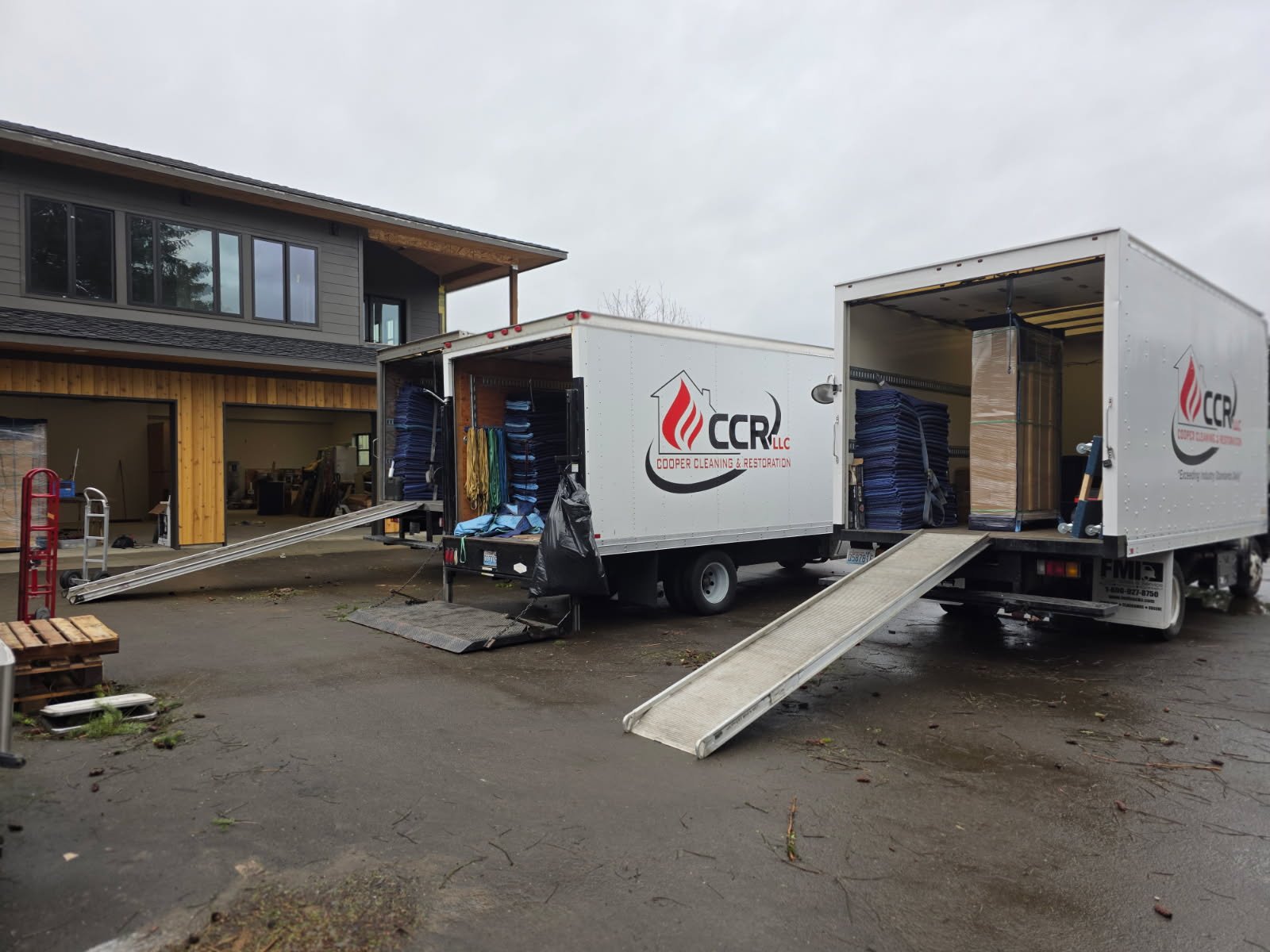 Two CCR box trucks open at a property, stacks of moving blankets and wrapped furniture inside