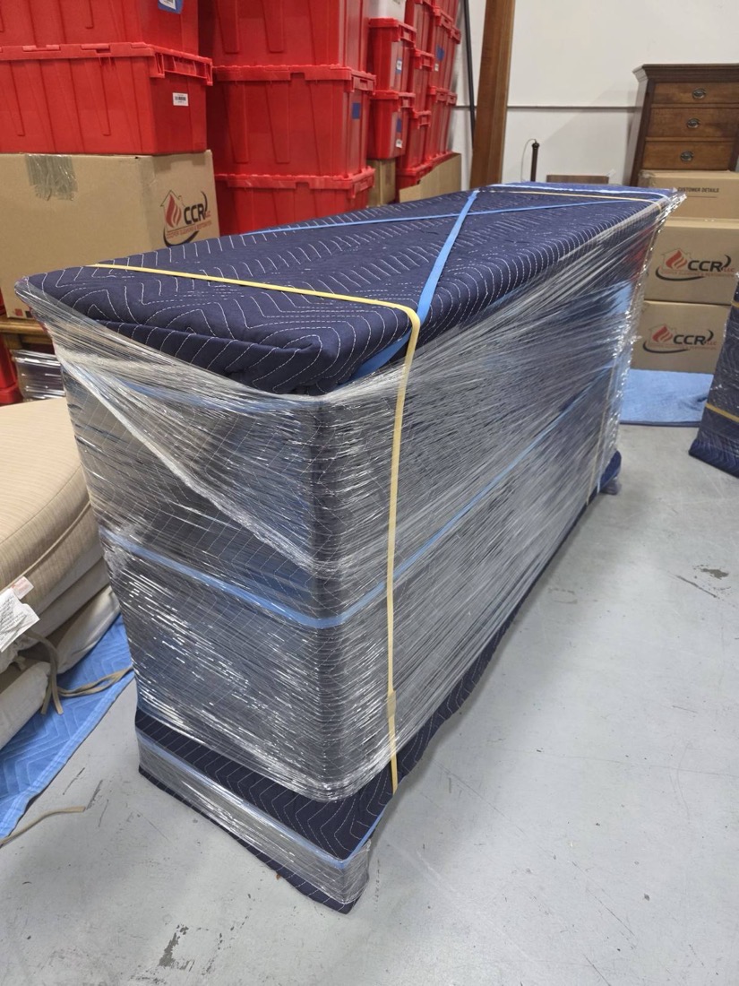 A long wrapped piece blanketed, shrink-wrapped and banded beside CCR’s red inventory totes