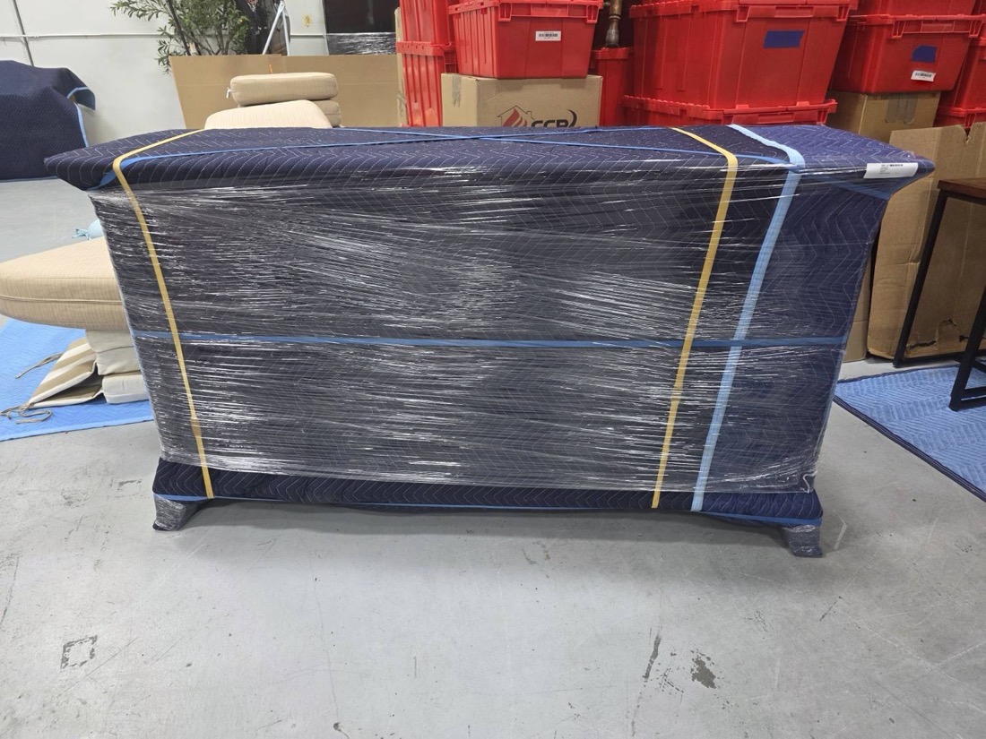 A chest of drawers wrapped and banded on the facility floor beside stacked CCR crates
