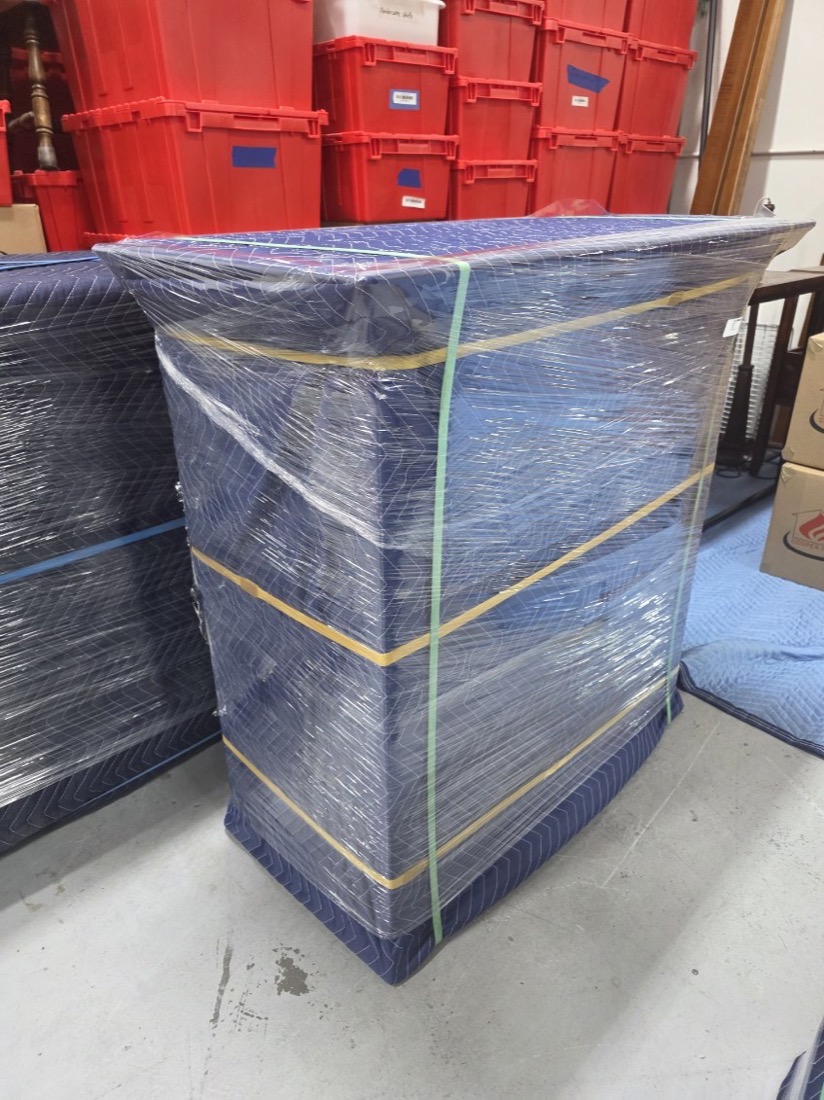 A tall wrapped cabinet strapped and standing in front of CCR&rsquo;s red inventory totes