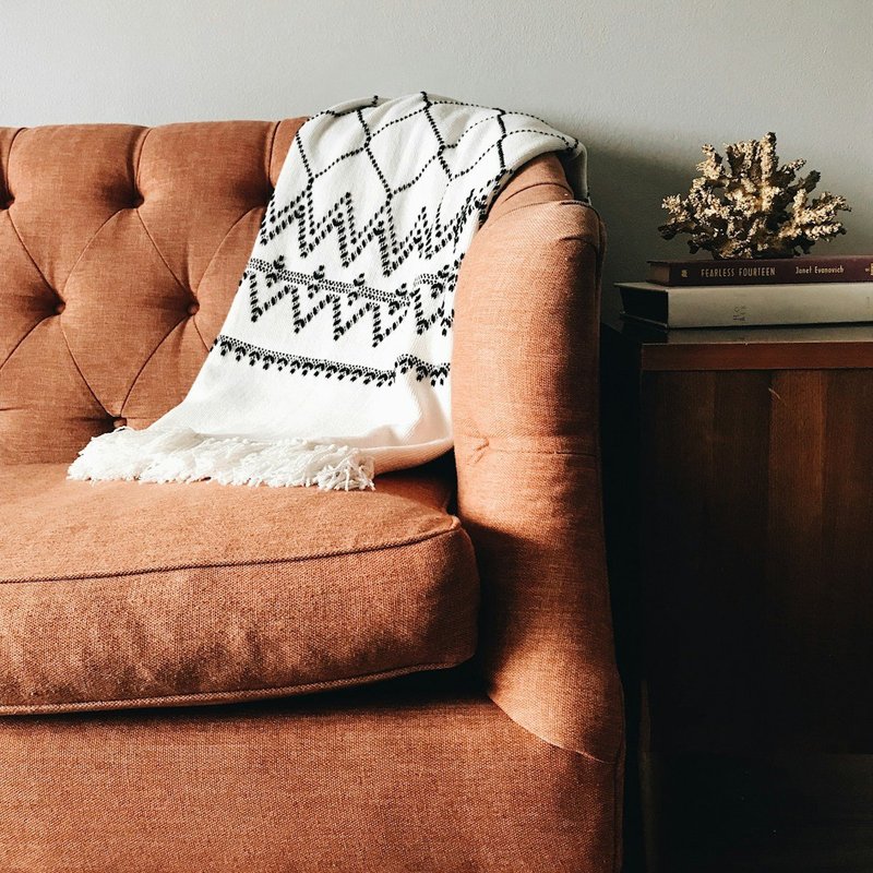 A fabric sofa with a woven throw blanket draped over the arm